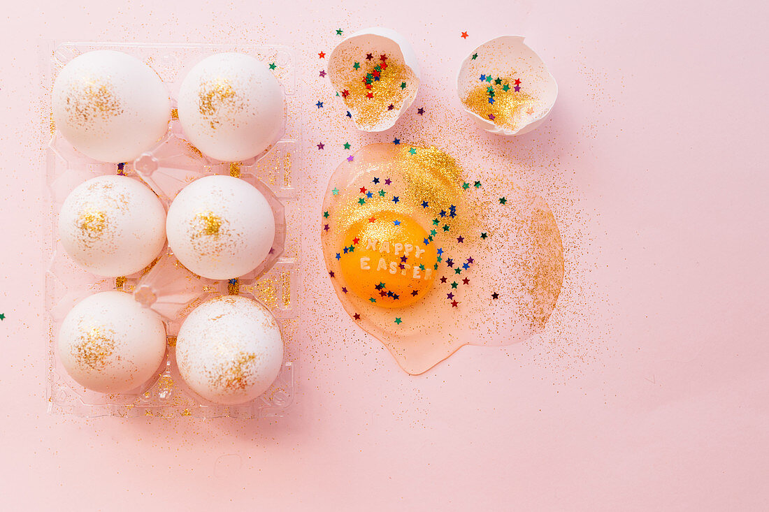 Osterstilleben mit aufgeschlagenem Ei, Goldglitter und bunten Sternchen
