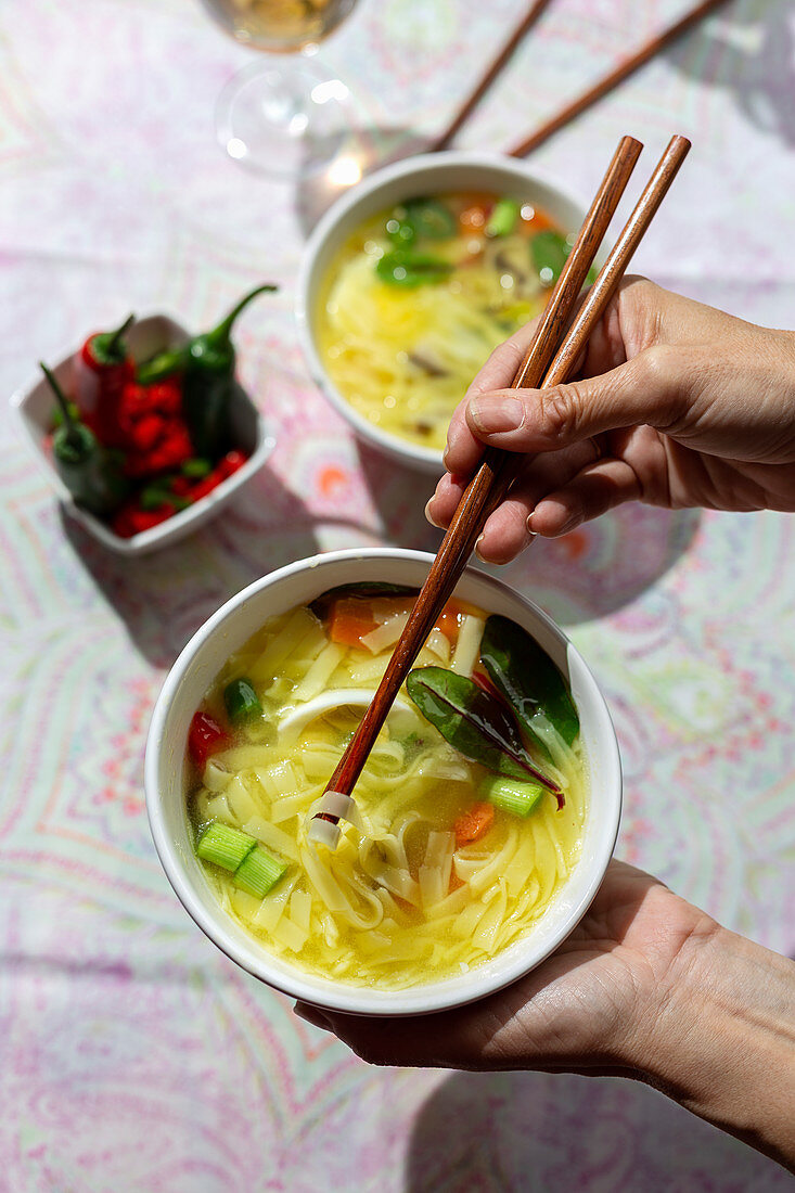 Hand holding a bowl of oriental ramen healthy noodles soup with shiitake, spinach, carrots, eggs and chillies