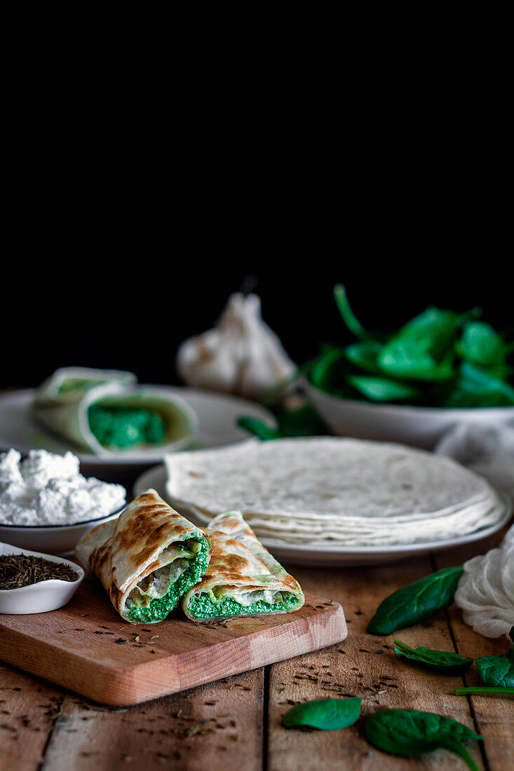 Tasty tortilla stuffed with puree of spinach on wooden table with ingredients