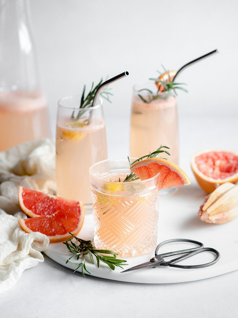 Three glasses of grapefruit cocktail on a marble tray with rosemary and grapefruit slices