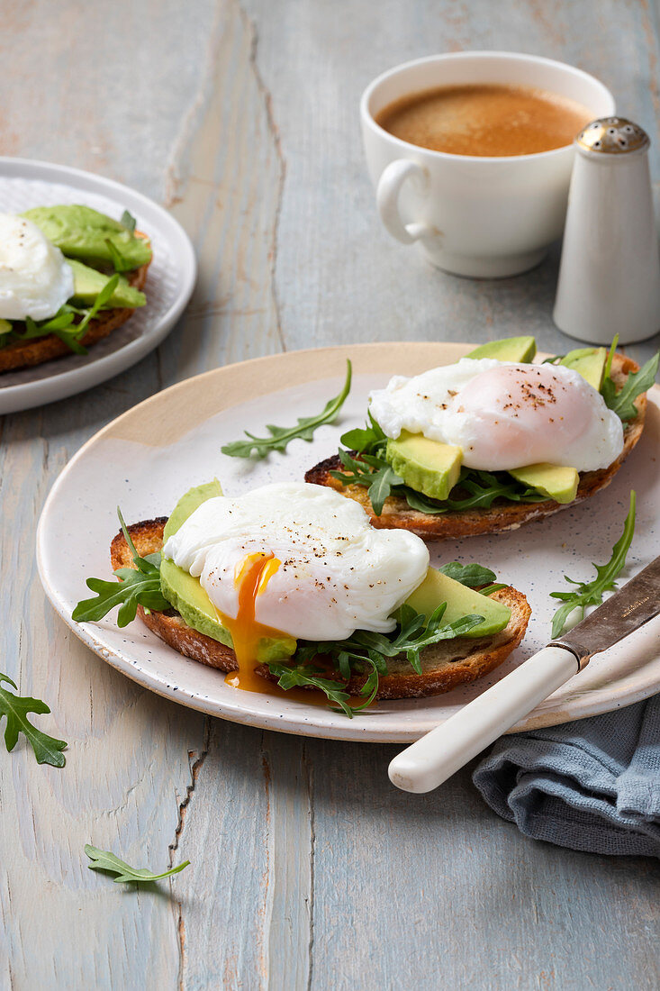 Toasts with avocado, rocket and poached eggs, coffee, rocket leaves