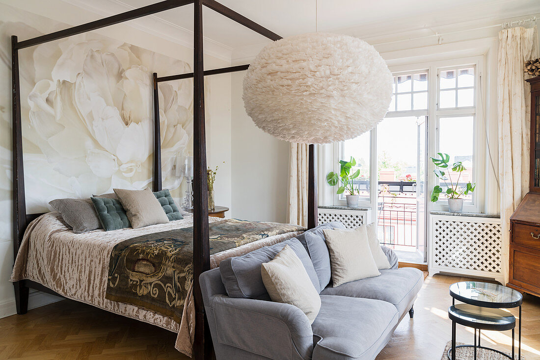 Velvet sofa at foot of four-poster bed in classic bedroom