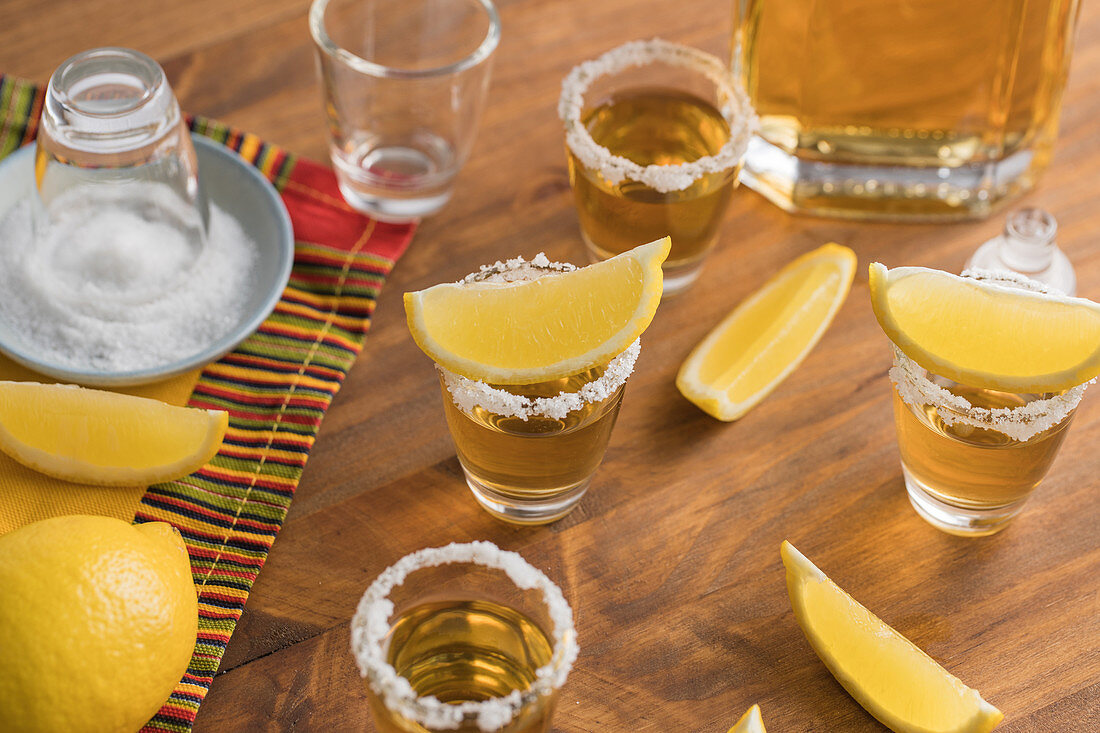 Glass shots of golden tequila with salty rim and slices of lemon on top