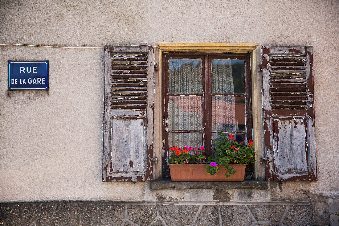 Geraniums in a window box with open shutters and a road name sign, Apach, France (tri-border area)