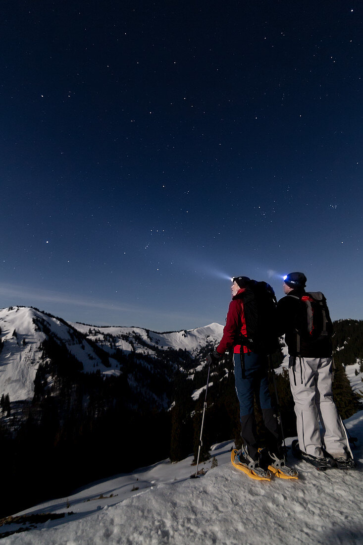 Snowshoe hikers in the moonlight on the summit near Bolsterlang in Allgäu, Germany