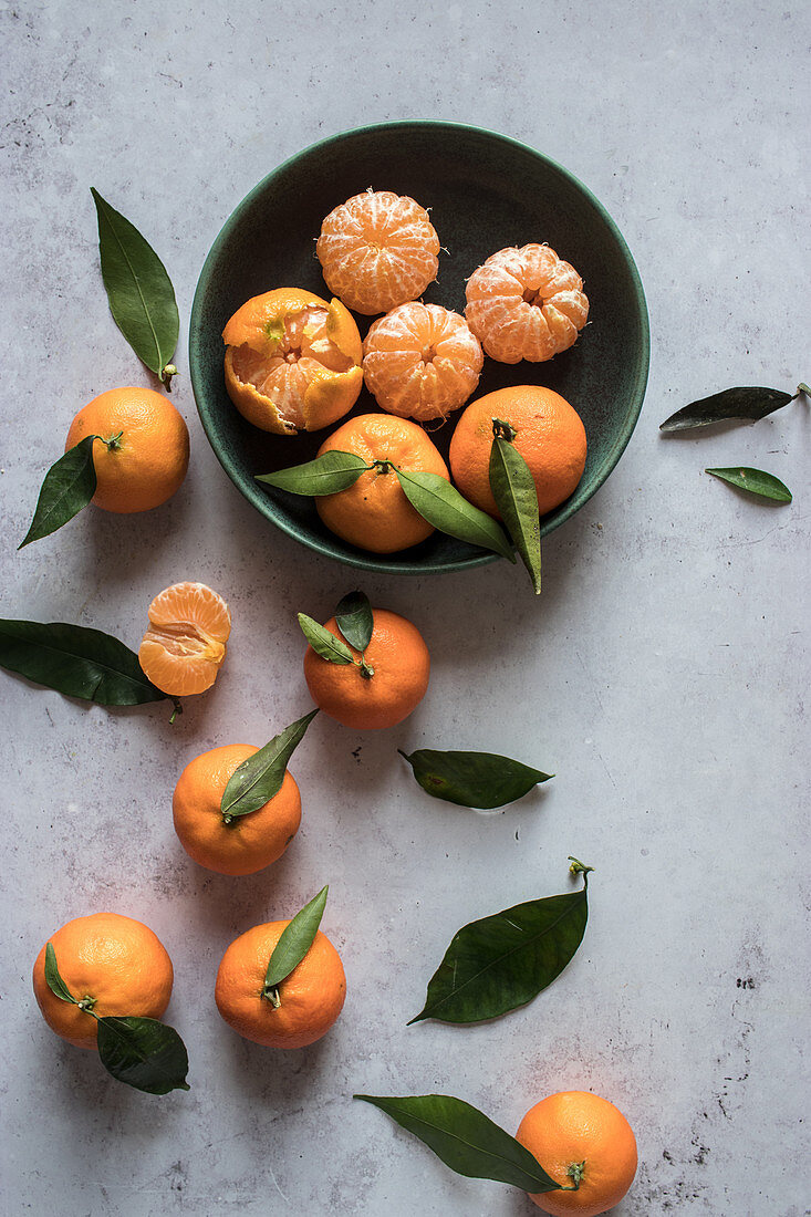 Fresh peeled tangerines and unpeeled fruits with green leaves