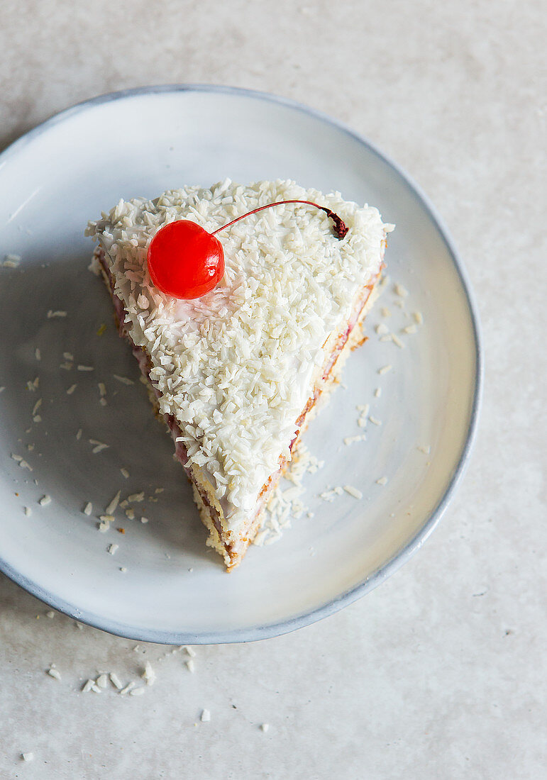 Slice of coconut cake with a glacier cherry on top