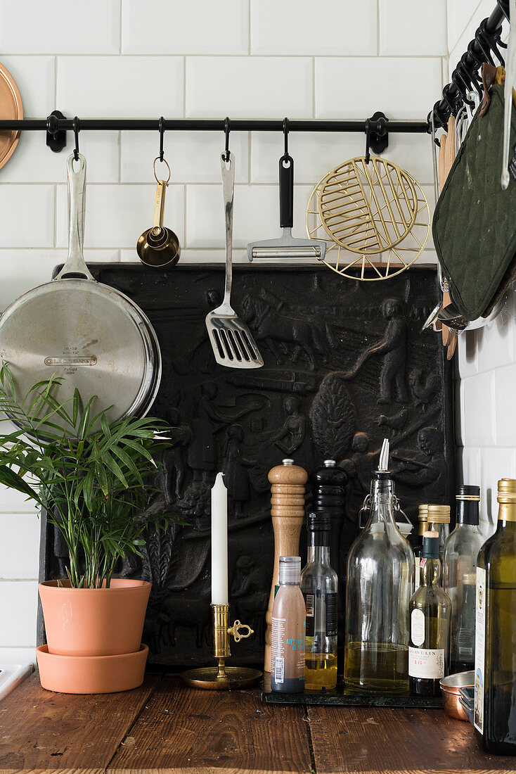 Kitchen utensils hung from hook rails above cast-iron, decorative fireback plate