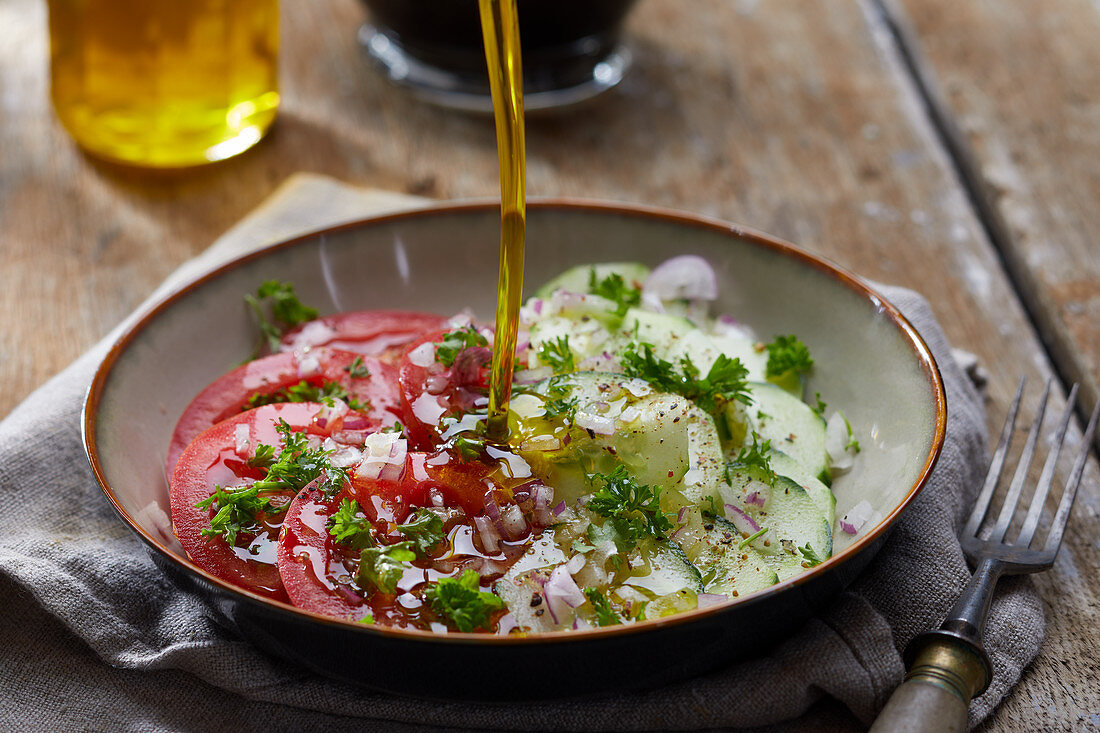 Pouring olive oil on a tomato and cucumber salad