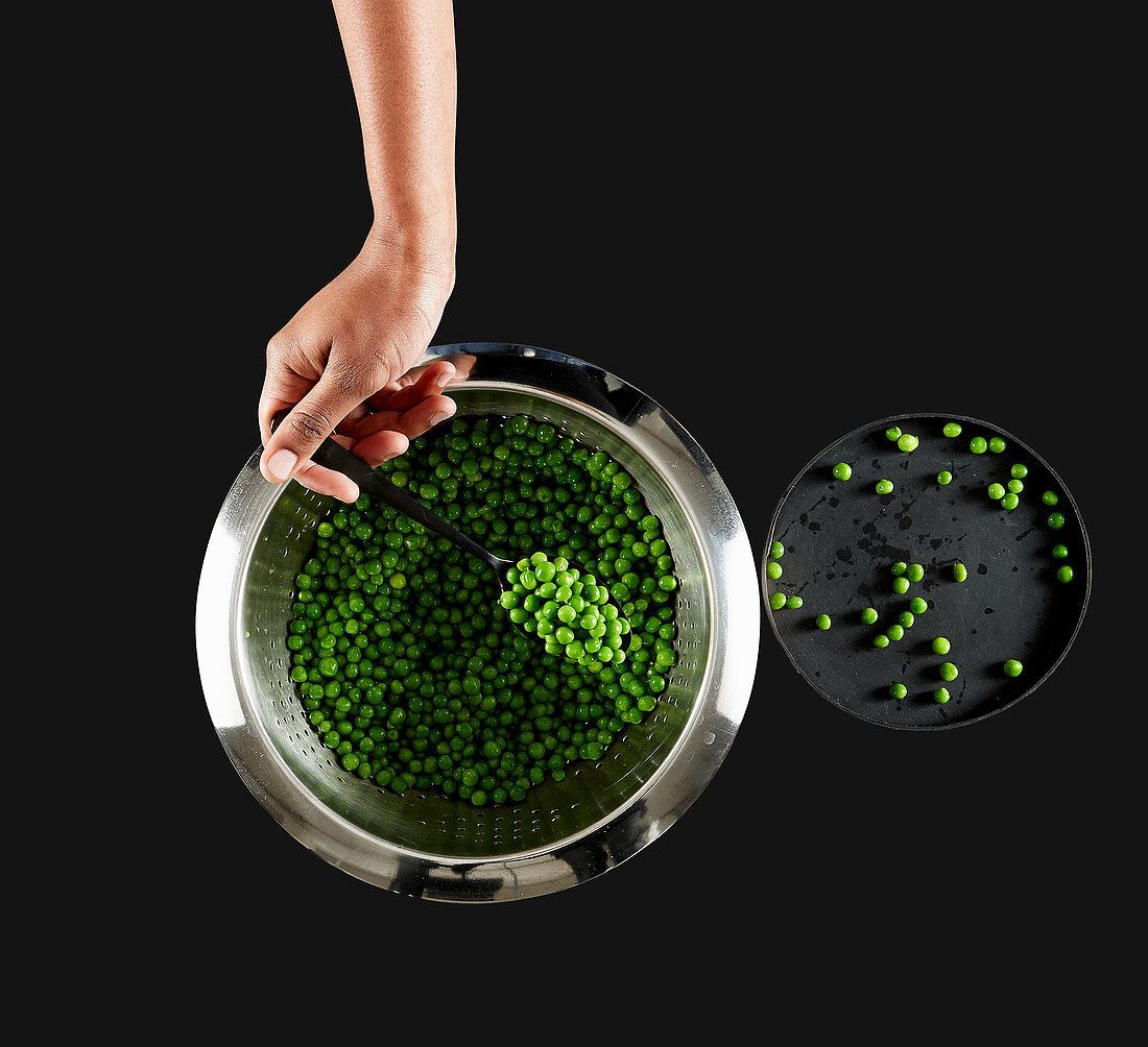 A hand spoons peas out of a metal colander