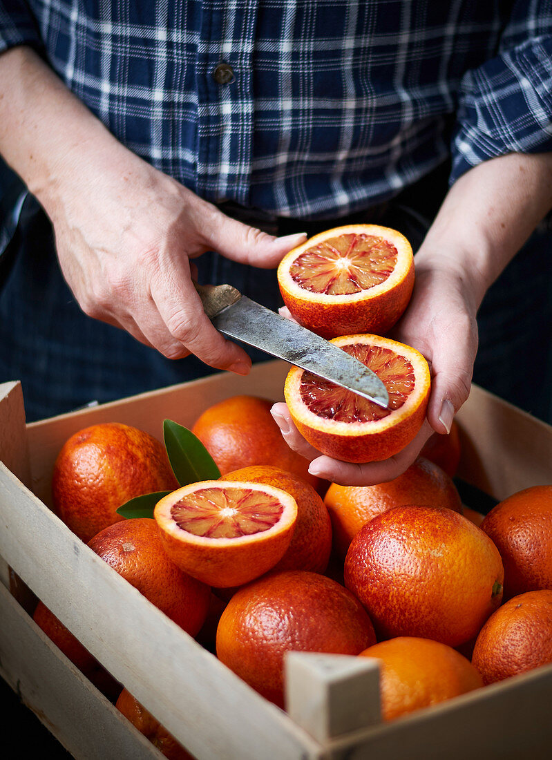 Man with a halved blood orange in front of a wooden box filled with blood oranges