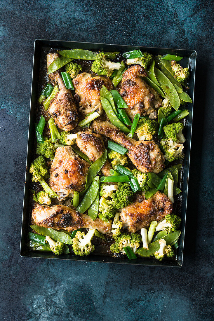 Satay chicken with green vegetables on a baking tray
