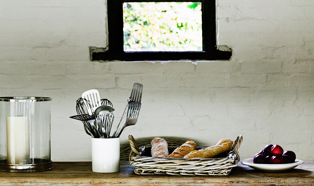 Küchenutensilien, Brotkorb und Plaumen auf Holztisch im Landhaus
