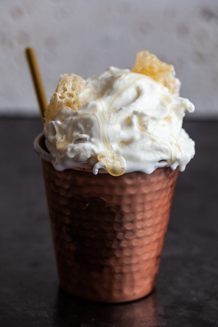 A copper cup filled with vanilla ice cream, topped with honey comb and drizzled with honey