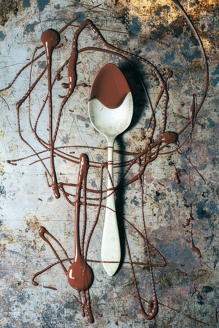 From above top view spoon with chocolate spilled over rustic metal surface background