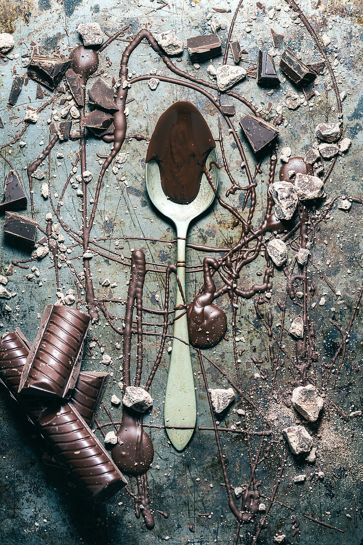 Geschmolzene Schokolade und Schokoladenstücke auf Löffel und rustikaler Metalloberfläche