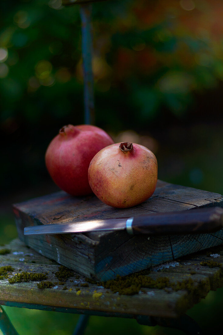 Zwei Granatäpfel mit Messer auf Holzblock