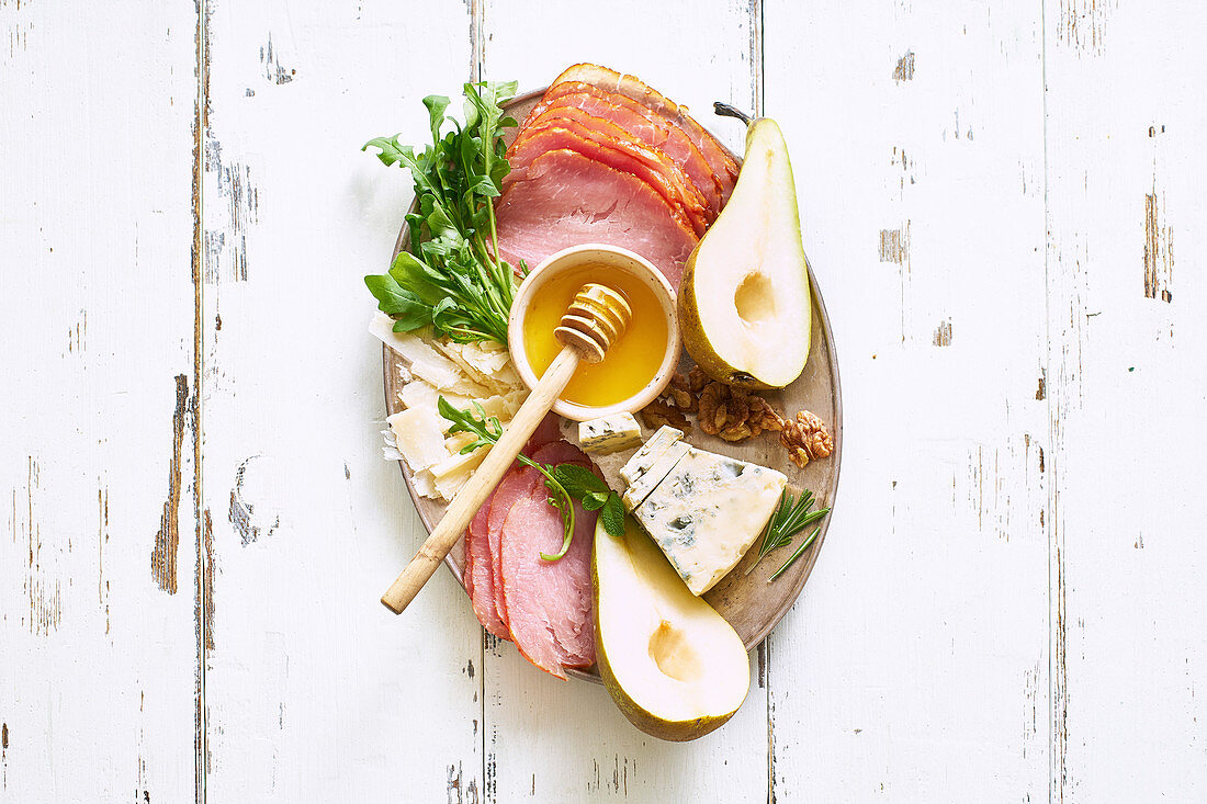 A plate of appetizers with cheese, fruits, nuts and honey on white wooden table