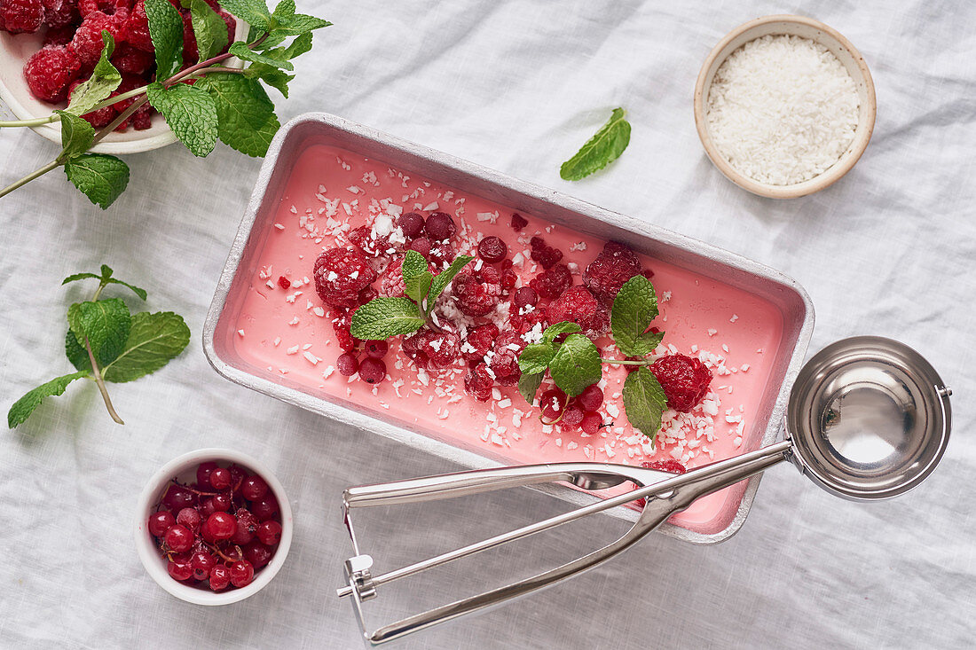 Pink ice cream with raspberries, mint and red currants on white linen tablecloth
