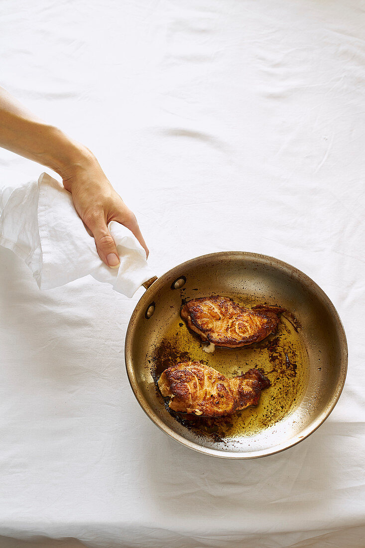 Hand hält Pfanne mit gebratenen Fischsteaks