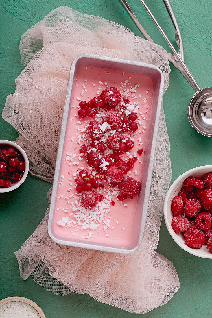 Pink ice cream with raspberries and red currants on green background