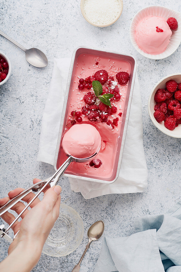 Female hand scooping pink ice cream with raspberries, mint and red currants