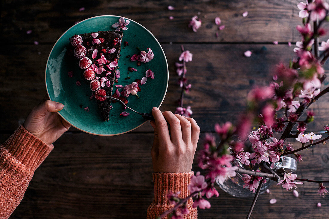 Ein Stück Mohnkuchen dekoriert mit gefrosteten Himbeeren und rosa Blüten