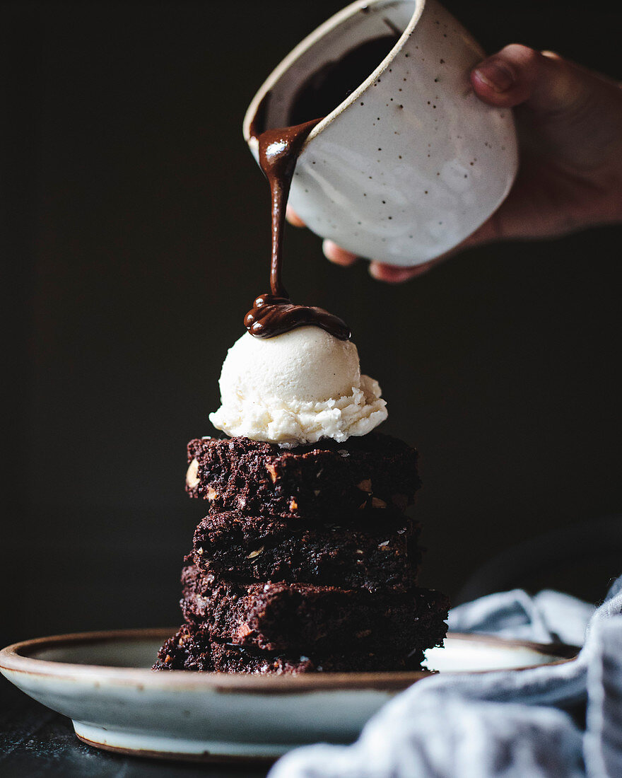 A stack of chocolate brownies, covered in ice cream and chocolate sauce