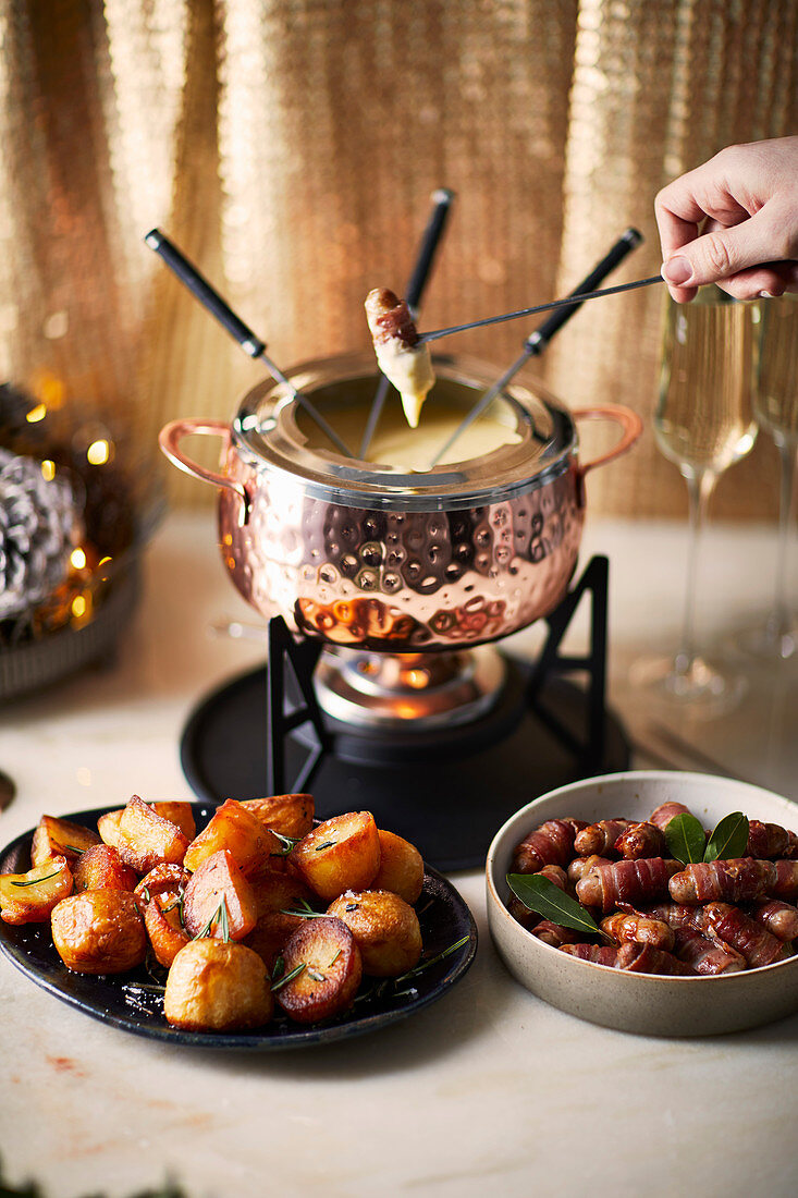 Cheese fondue with roast potatoes and sausages in bacon