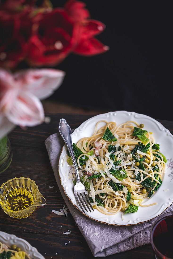Spaghetti with kale, green peas, panceta and Parmesan cheese served on a plate on a rustic wooden table