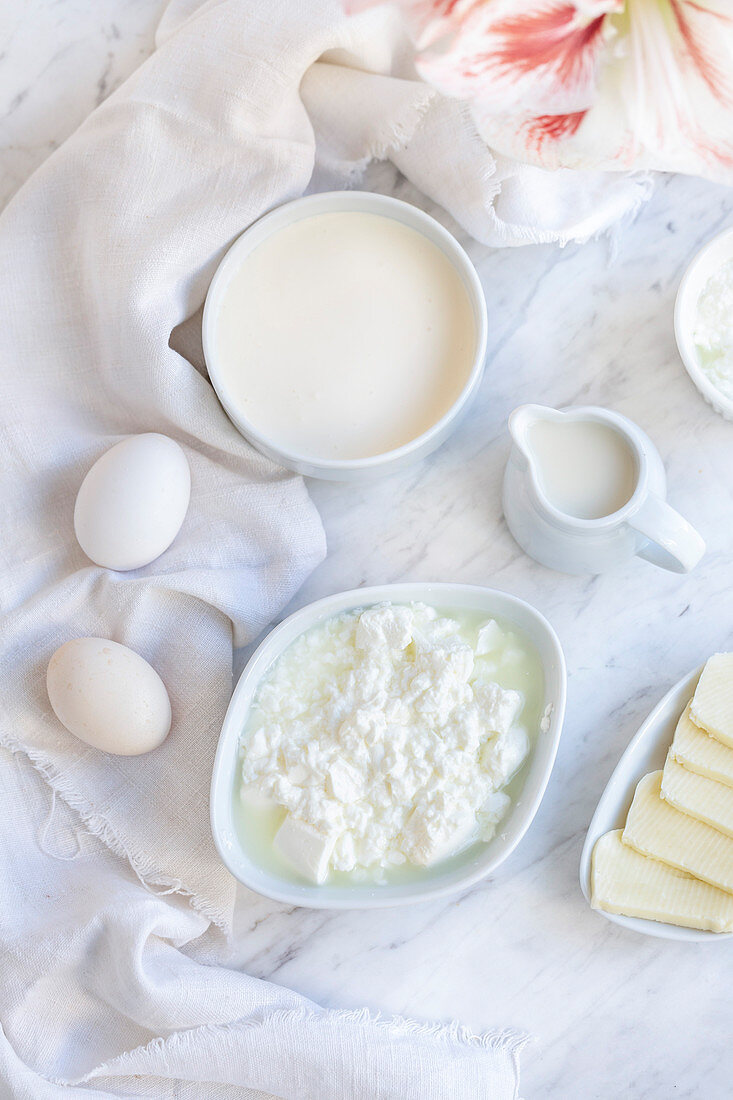Frischkäse, Milch, Sahne und weiße Eier auf weißem Marmortisch