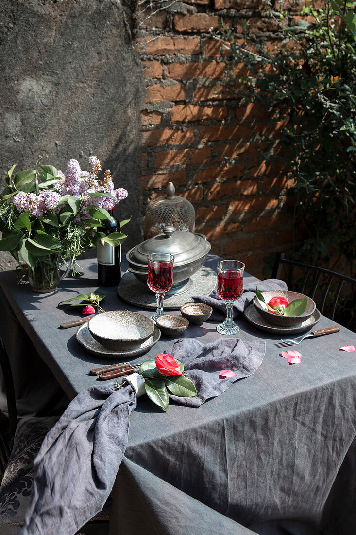 Mediterran gedeckter Esstisch auf Terrasse mit Blumenstrauß und Rotwein