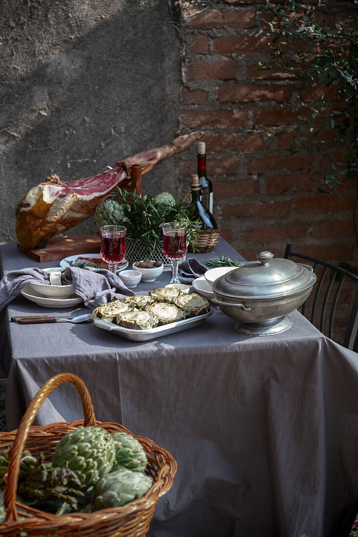 Mediterran gedeckter Tisch mit Serranoschinken, gebackenen Artischocken und Wein