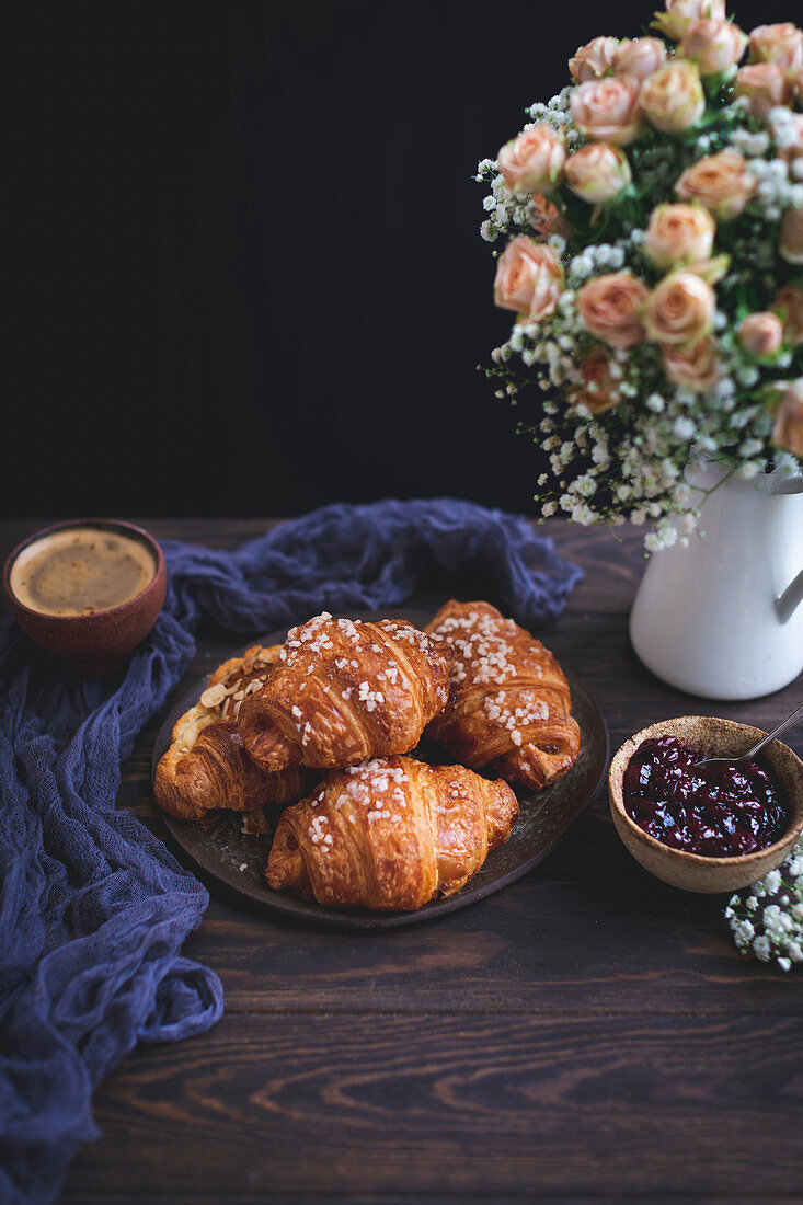 Croissants, Marmelade und eine Tasse Kaffee auf rustikalem Holztisch