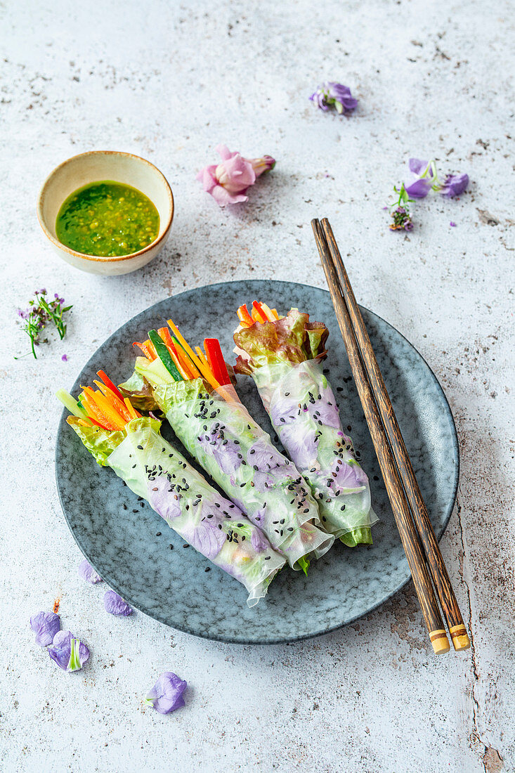 Vegan spring rolls with edible flowers in rice paper and green chili dip