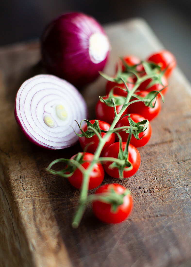 Bunch of fresh ripe tomatoes cherry and cut red onion bulbs placed on wooden cutting board