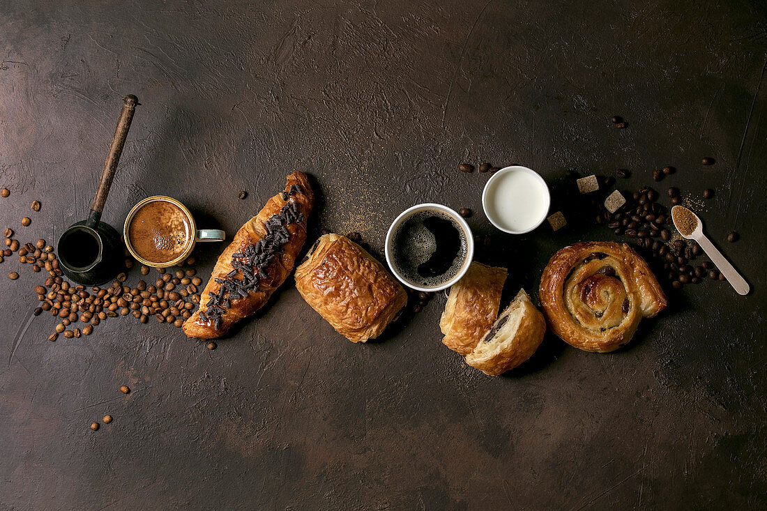 Variety of traditional french puff pastry raisin and chocolate buns, croissan, cups of coffee and milk