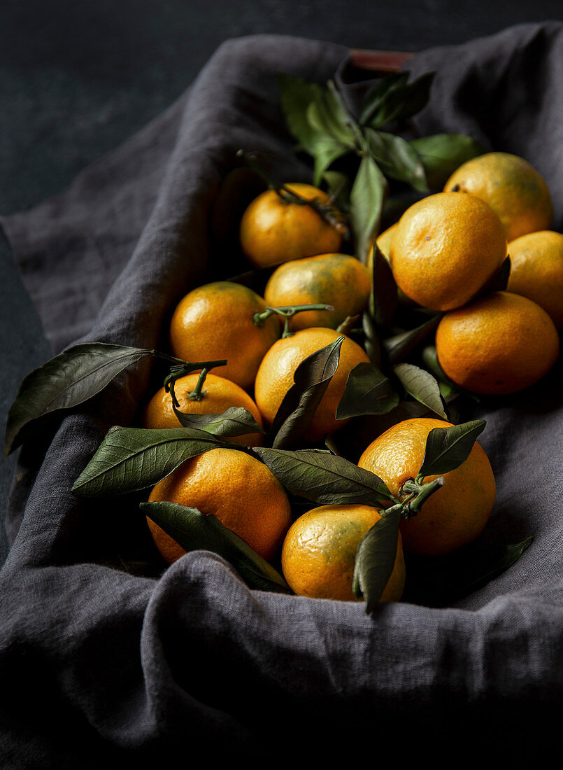 Frische Mandarinen mit Blättern auf grauem Leinentuch