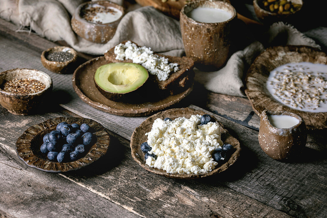Healthy breakfast. Variety of breakfast dishes sprouted wheat, yogurt, kefir, cottage cheese, avocado, rye bread, seeds, nuts and berries assortment in ceramic bowls over rustic wooden table.