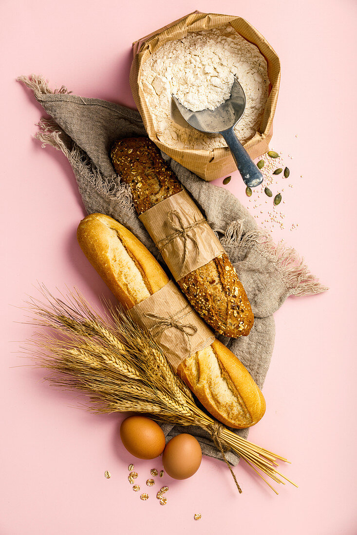 Top view of white and wholegrain baguettes and baking ingredients over pink background