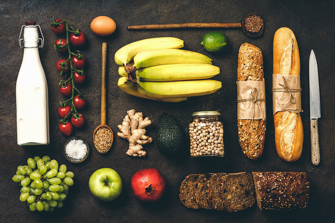 Flat lay of healthy food - milk, bread, fruits, vegetables, grains and legumes on rustic background