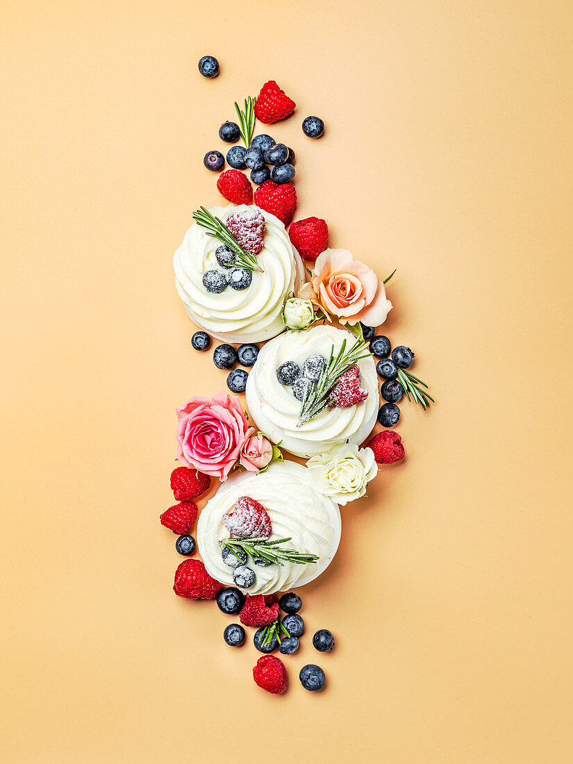 Mini-Pavlovas dekoriert mit Beeren und Rosenblüten auf apricotfarbenem Untergrund