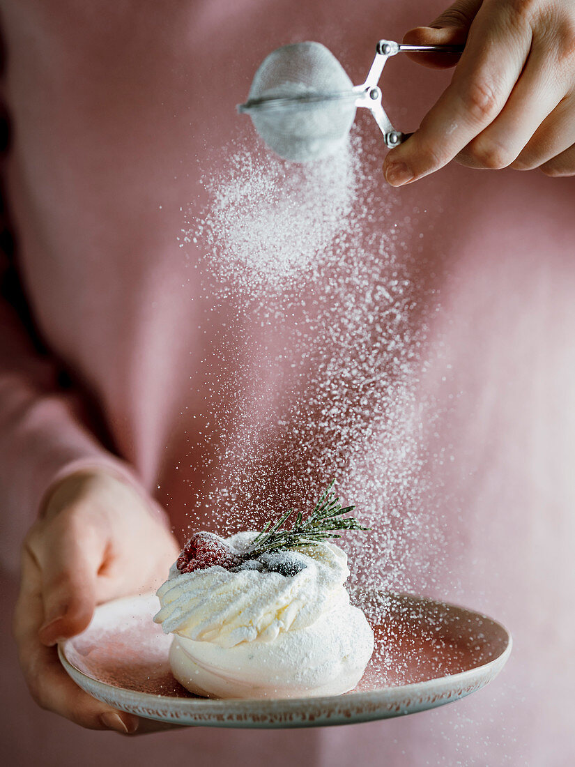 Frau bestaubt Mini-Pavlova mit Puderzucker