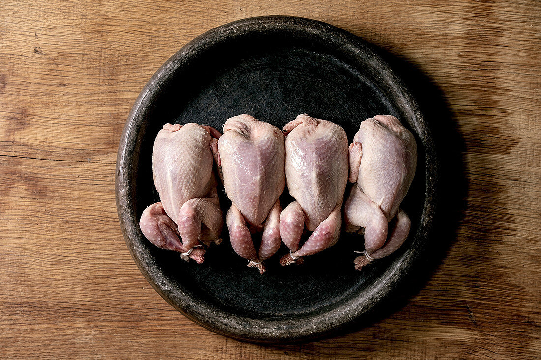 Raw uncooked quails ready for marinat in clay tray over wooden background