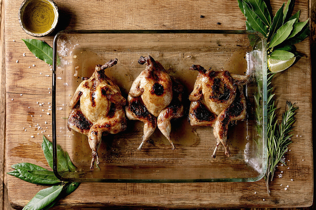 Roasted grilled butterfly quails in glass baking tray with greens, salt and olive oil