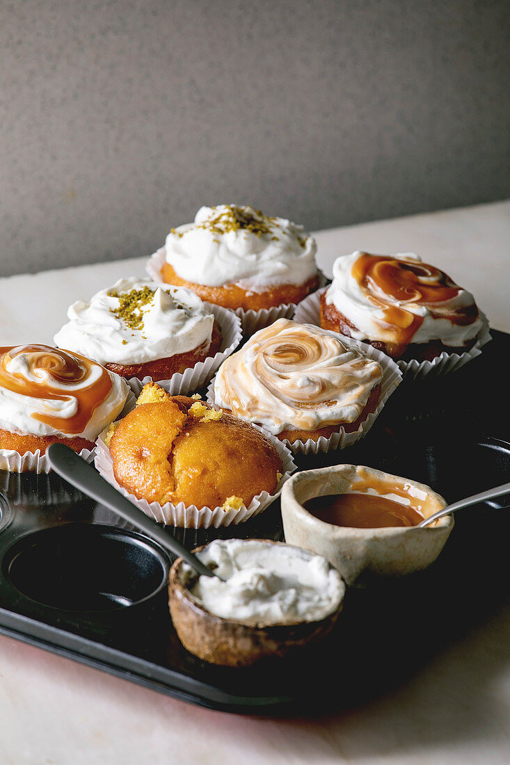 Homemade citrus oranges or clementines sweet muffins cupcakes in baking tray with different cream, pistachio, caramel toppings in bowls