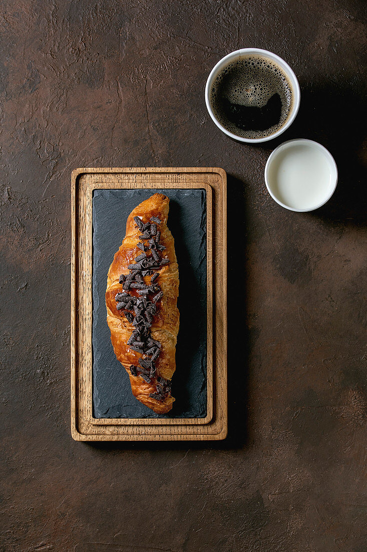 Traditional french puff pastry and chocolate, croissant on slate wooden board with paper cups of coffee and milk