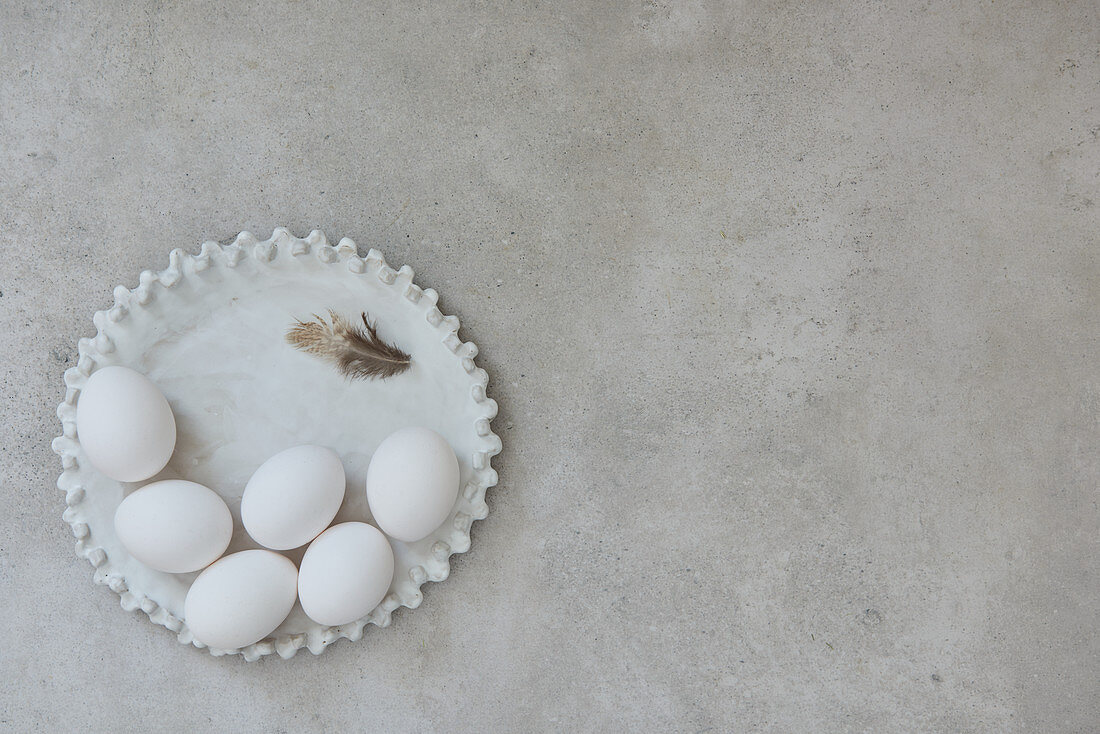 Ceramic plate with white eggs and a feather