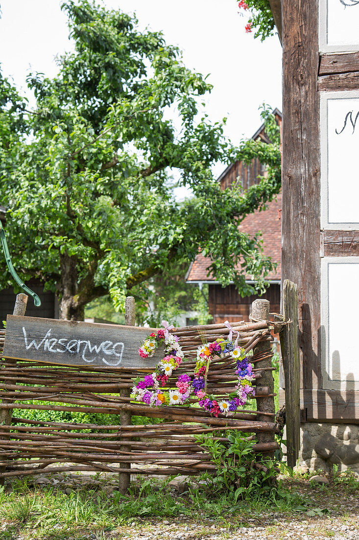 House number made from wreaths of flowers hung on wattle fence