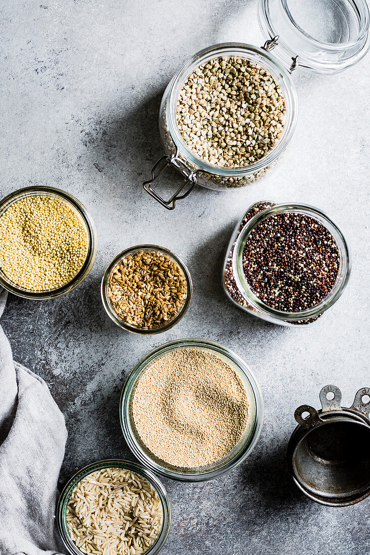 Buchweizen, brauner Reis, Quinoa, Hirse, Amarant und Leinsamen in Glasgefässen